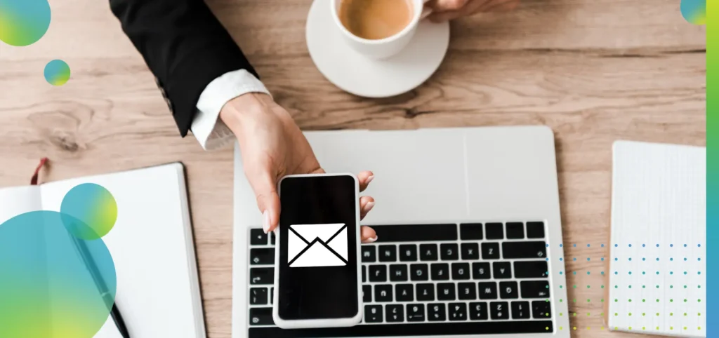 Top view of businesswoman holding smartphone with envelope on screen and cup with coffee near laptop