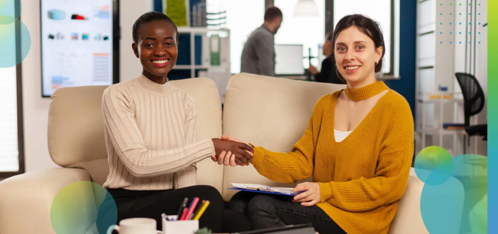 Diverse women looking at camera smiling, shacking hands.