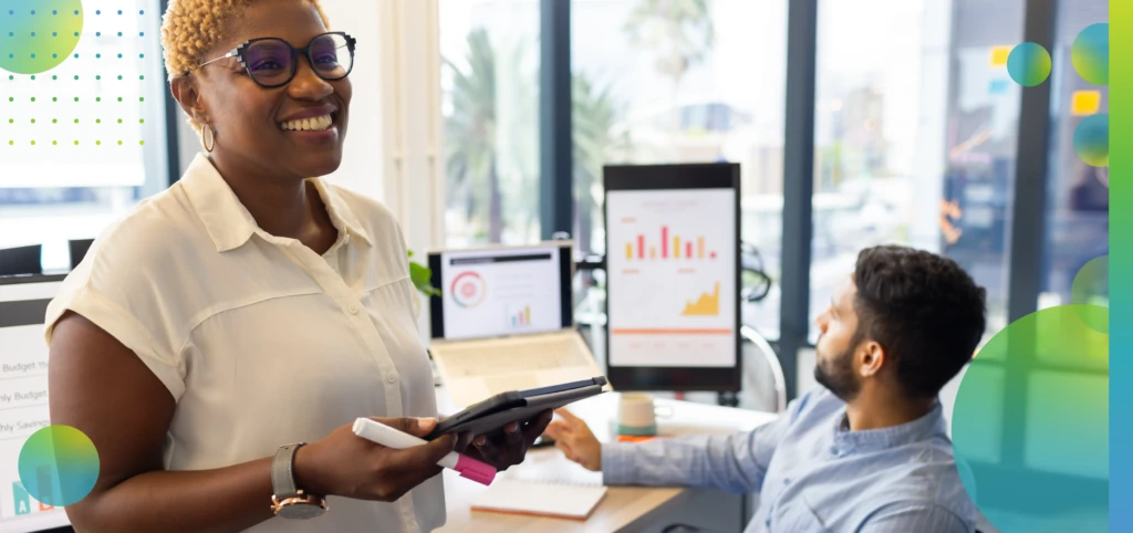 Presenting data on tablet, businesswoman smiling as colleagues discuss graphs in office.