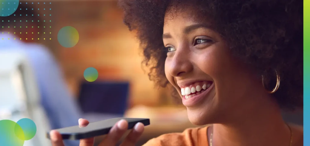 Close Up Of Young Smiling Businesswoman Working At Desk In Office Talking Into Mic Of Mobile Phone.